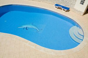 Pool Plastering ca "Clear blue swimming pool with a traditional tile floor with dolphin mosaic, stairs, and sun bed in the garden. Some copyspace at the bottom of the picture."