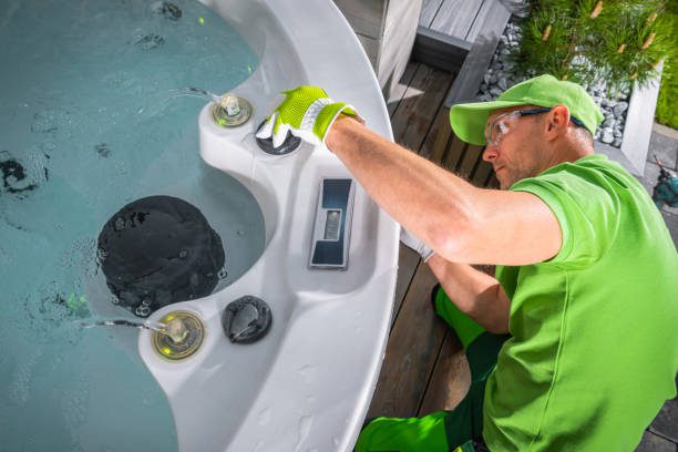 A professional pool remodeler wearing a green shirt and gloves repairs a hot tub, demonstrating expert pool remodeling skills and attention to detail.