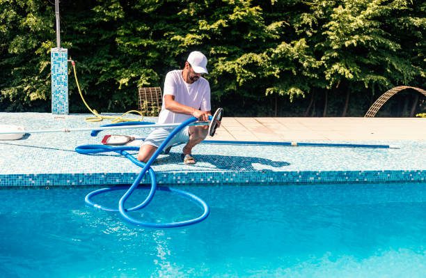 Experienced pool remodeler in flip flops cleaning the swimming pool with a net, standing poolside with special equipment for maintenance.