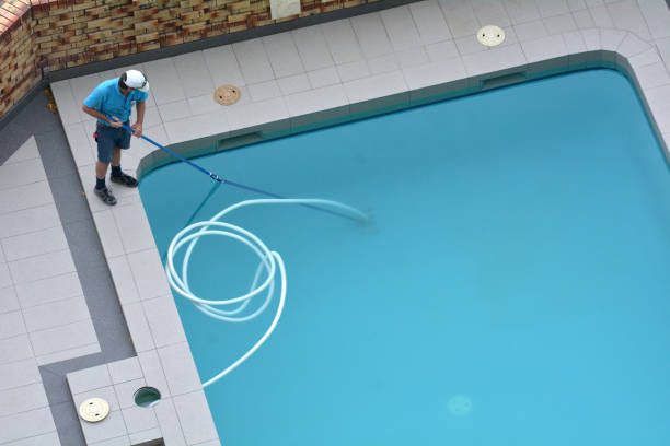 Aerial view of a professional performing pool remodeling by cleaning and maintaining a backyard swimming pool.