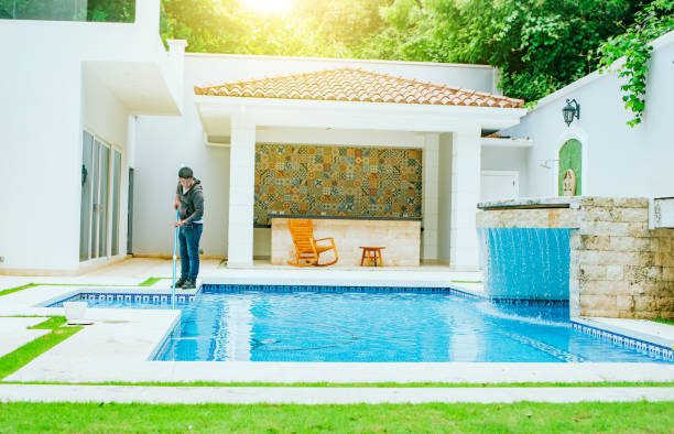 A man stands beside a serene pool in a well-maintained backyard, enjoying the tranquil outdoor setting after a pool remodeling project.