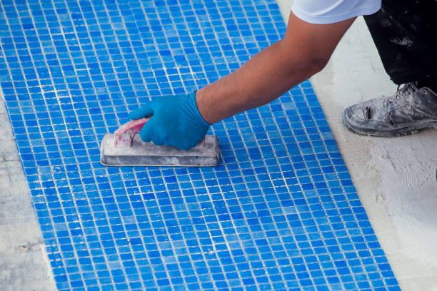 Worker laying tile in the pool as part of a pool replastering service in Ontario, CA, ensuring a smooth and durable surface.