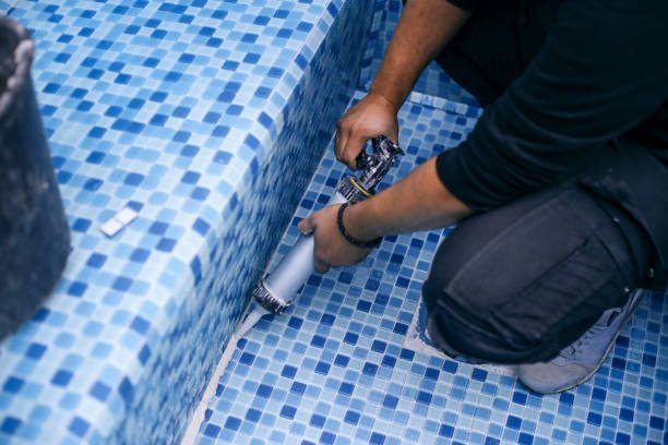 A man repairs a blue tile pool surface using a specialized tool, showcasing skilled craftsmanship in pool replastering service Ontario CA.